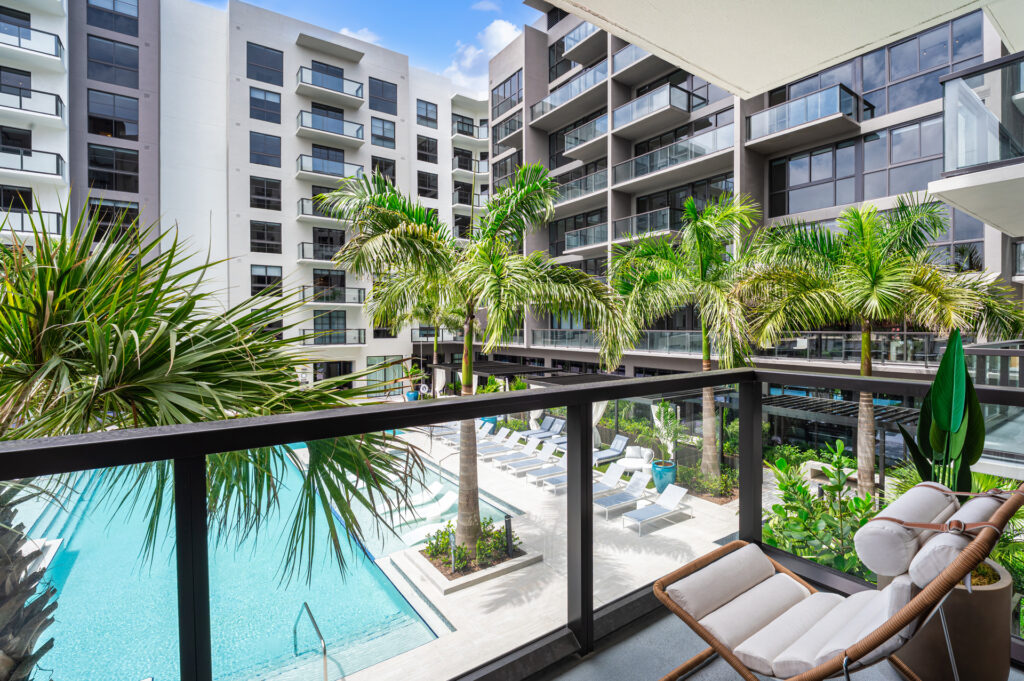 Private balcony at Manor Biscayne luxury apartments in North Miami, FL — lounge seating with views of the resort-style pool and palm-lined courtyard